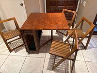 Table with both drop leaves partially extended and four folding chairs arranged around