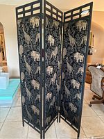 Full view of the folding screen standing open showing all three panels with black metal frame and black fabric featuring gold imprinted animal designs.