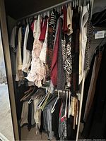 Closet rod with assorted women's tops and some dresses, various colors and patterns, hung on hangers