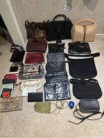 Wide shot showing all assorted purses spread on carpet including wicker handbag, black structured bags, clutches, fabric wallets, and small purses.