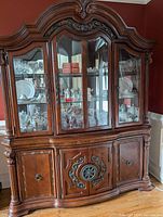 Front view of the wooden china cabinet with carved details, glass doors revealing display items.