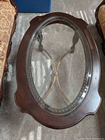 Top view of coffee table showing oval glass inset surrounded by dark wood frame.