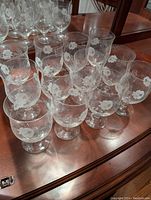 Set of 12 stemmed crystal glasses arranged on a wooden surface, showcasing their etched floral design and overall condition.
