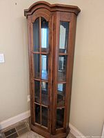 Full view of tall wooden curio cabinet with glass front door and multiple glass panes, brown finish.