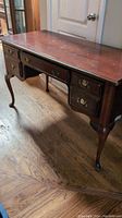 Full view of wooden executive desk showing polished top surface with scratches, five drawers with brass hardware, and Queen Anne style curved legs.