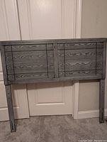Gray wooden full size bed headboard with two panel design, standing upright against a white door.