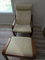 Front facing photo of IKEA leather chair and matching ottoman, showing light tan leather upholstery and wooden frame on light wood floor.