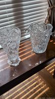 Two heavy lead crystal vases placed side by side on a wooden surface near window blinds, showing overall shape and design details.