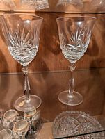 Two lead crystal wine glasses with detailed starburst cut pattern on the bowl, faceted stems, and round bases on a wood surface