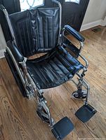 Manual wheelchair in black and chrome with padded seat, backrest, and armrests, showing standard footrests.