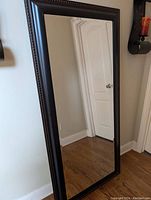 Front of the mirror standing against the wall showing the large reflective surface and dark brown detailed frame