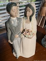 Front view of bride and groom porcelain figurine with bride holding flowers.