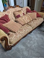 Full view of one vintage sofa with patterned fabric upholstery and multiple cushions in floral and striped designs, featuring carved wooden armrest.