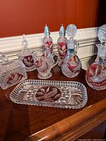 Full set of Nachtmann Red Bird crystal including 2 decanters, salt & pepper shakers, candy dish, sugar bowl with lid, milk pitcher, and tray on wood surface