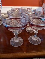 Close-up of several crystal champagne glasses showing red bird etched design and pattern on the bowl with short stems.