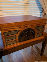 Full view of the wooden vintage-style audio system unit on a wooden side table near window with blinds.