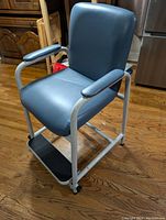 Full view of the vinyl chair showing blue vinyl seat and backrest, armrests, metal frame, and attached footrest.