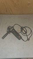 Photo shows the Black & Decker 4 inch electric grinder from above with side handle and power cord coiled nearby on a light surface.