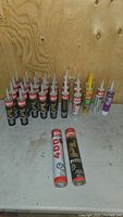 View of the lot showing 27 unopened construction adhesive tubes from Lepage, Sika, and Sakrete in various sizes and formulas.