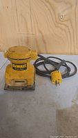 Front view of Dewalt yellow palm grip sander with power cord and plug visible, showing wear and dirt on the tool.