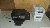Black Epson ET-4550 bulk ink tank printer with trays extended next to seven bundles of copy paper in white packaging.