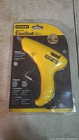 Front view of the Stanley GlueShot glue gun in unopened yellow and black branded packaging showing the product name, features and usage instructions.