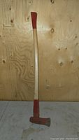 Full view of the splitting maul showing the 41-inch wooden handle with red painted grip and the red painted metal head.