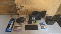 Overview of lot items on floor including power bar, smoke alarm box, felt furniture pads, candle holder, wall trays, basket, USB keyboard, USB speaker, power block, and wall clock