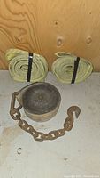 Two rolled yellow recovery tow straps positioned side by side with black bands, and a coiled black tie down strap attached to rusty metal chain and hook on a white surface.