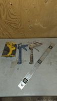 Photo showing two used metal caulking guns, a 2-foot metal level with three bubble vials, all used condition