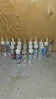 Multiple new and unopened tubes of silicone and caulking sealants standing upright showing varied brands and labels.