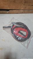 Red siphon tool with flexible black hose packaged in clear plastic, top view.