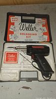 Top view of Weller soldering kit inside molded plastic case with soldering gun and box of solder visible
