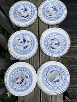 Top view of 6 place settings showing stacked plates, cups and saucers arranged and photographed outside on wood surface.