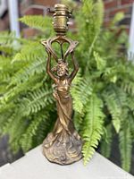 Front view of the gilded Art Nouveau lamp base showing the female figure holding the circular element under the lamp socket.