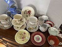 Full lot view showing variety of plates, cups, saucers, and mugs on wooden surface