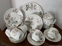 Full view of dessert set showing cake plate, dessert plates, cups with saucers, and cookie barrel, all with floral and gold accents.