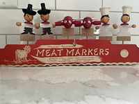 Front view of the six hand painted wooden meat markers in original red packaging labeled 'Meat Markers'.