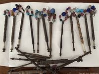 Entire collection of approximately 15 wooden lace bobbins with colorful beads on a white background showing shapes and bead details.