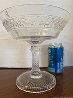 Full view of clear pressed glass compote with open bowl shape, ribbed foot, and decorative embossed pattern.