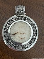 Front view of large sterling silver pendant with neutral stone and intricate swirl silver detailing around bezel and bail featuring a heart motif.