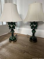Pair of green glass Victorian Lustres table lamps with off-white silk shades on wood floor