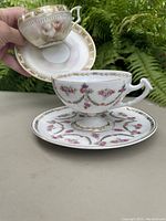 Two porcelain cup and saucer sets displayed outside, showing intricate floral patterns and gold detailing.