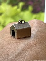 Close-up side view of the sterling silver doghouse pendant showing its shape and loop for chain attachment.