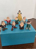 Set of eight miniature vintage Disney Snow White and the Seven Dwarfs figurines displayed on a blue box.