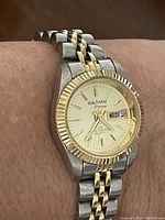 Waltham Prestige wrist watch on wrist showing day and date functionality. Two-tone stainless steel band with gold accents, fluted gold-tone bezel, silver dial with gold markers and hands.