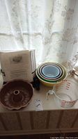 Full view of the bakeware including mixing bowls, bundt pan, Pyrex measuring cup, electric warmer with manual on a windowsill.