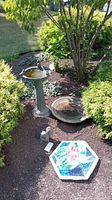 Outdoor garden scene showing all items: tall birdbath with scalloped basin, separate basin on the ground, colorful hexagonal mosaic stepping stone, and the small squirrel statue near stone.