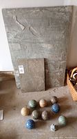 Full lot showing slate slabs at back with nine ceramic balls arranged in front on floor.