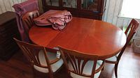 Oval wooden dining table with 4 matching chairs around it and a leaf placed on the table.